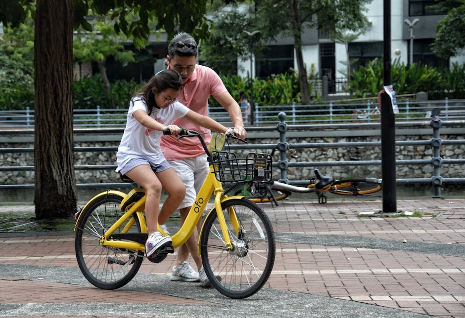 Father teaches daughter to ride a yellow bicycle in a Singapore park. Bonding moment.
